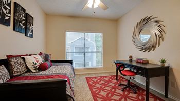 a bedroom with a bed, desk, and ceiling fan at Wilson Crossing Apartments in Cedar Hill, Texas